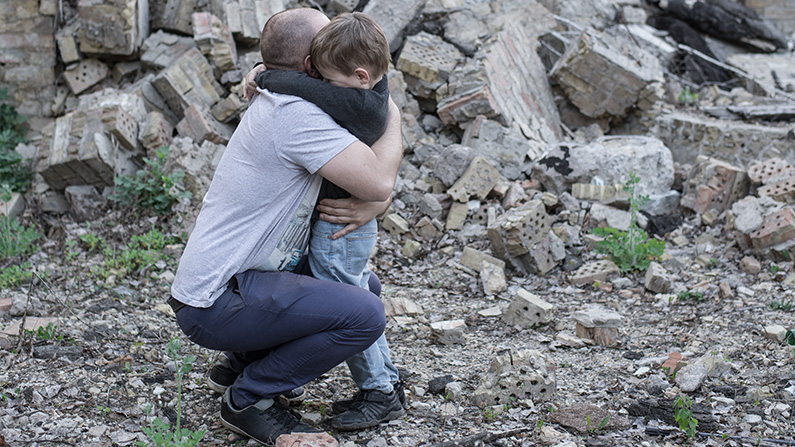 Vater und Sohn umarmen und trösten sich, vor ausgebombten Häuser